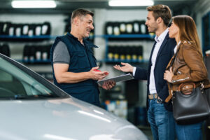 Young happy couple talking to car mechanic in auto repair shop. Pièges et risques à éviter lors de l’achat d’une voiture de prestige